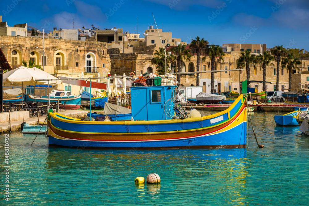 Marsaxlokk, Malta - Traditional colorful maltese Luzzu fisherboat at the old village of Marsaxlokk with turquoise sea water and palm trees on a summer day