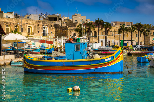 Marsaxlokk  Malta - Traditional colorful maltese Luzzu fisherboat at the old village of Marsaxlokk with turquoise sea water and palm trees on a summer day