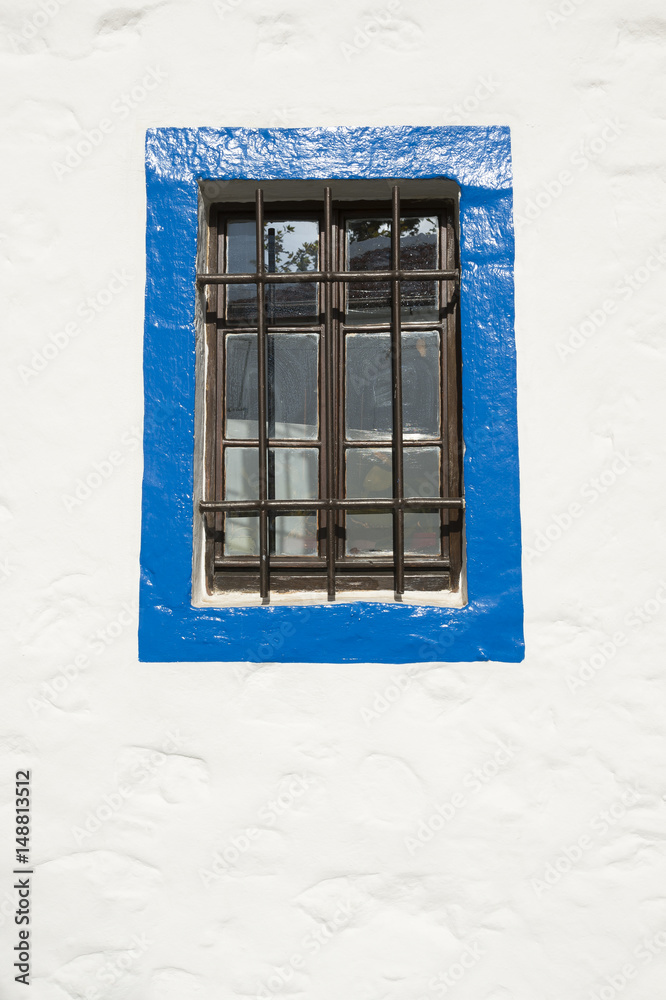 Fototapeta premium Simple window with iron bars surrounded by blue border on a white stucco wall