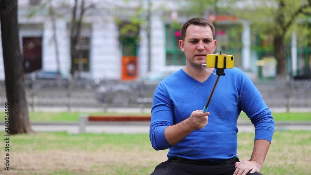 Blogger is reporting on the street. Young brunette man taking selfie with stick in ultra hd format