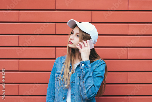 Stylish student in cap talking on phone pink color on a red background. Young beautiful woman hipster use a mobile phone. Looking towards
