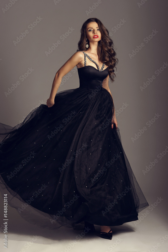 Young beautiful woman standing and posing in black ball gown on white gray  background. Fashion style portrait of girl with long curly brunette hair  Stock Photo | Adobe Stock
