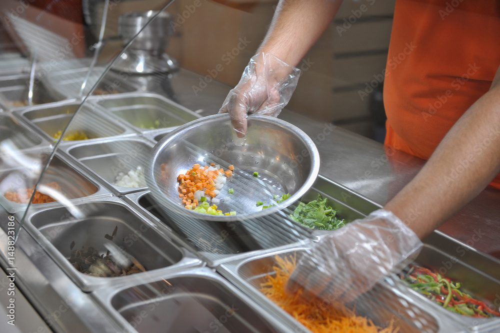 the cook puts pieces of vegetables for salad in a bowl. tray with assorted for salad in the window of a fast food restaurant