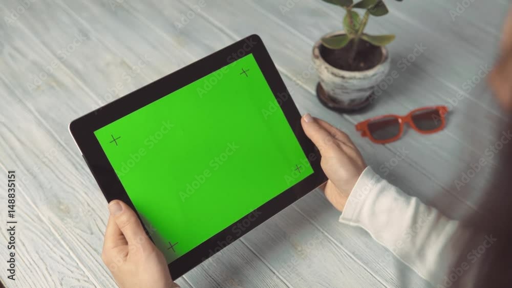 Indoor shot of a woman holds tablet pc with marked green screen on white wooden table, slide and pick gestures