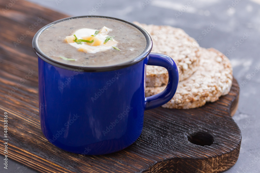 Creamy mushroom soup puree in a blue mug with crisps on wooden board. Healthy dinner. Vegetarian food. Clen and healthy eating consept.
