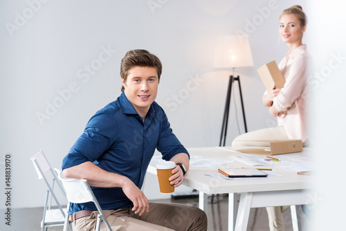 portrait of smiling businessman with coffee cup at workplace with colleague near by photo