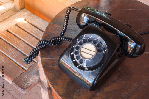 Old black phone with dust, circle dialpad and scratches on wooden retro desk. Vintage desk telephone concept. photo