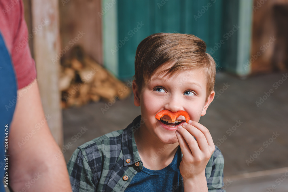 Cute little boy holding pepper slice as moustache and looking away Cute little boy holding pepper slice as moustache and looking away