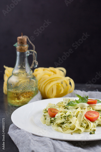 Still life - Homemade pasta from basil and arugula with green pesto in a white plate on a dark background.
