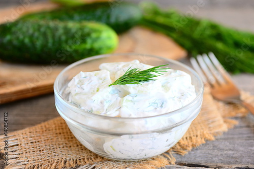 Creamy cucumber dill salad. Homemade cucumber salad in a plate. Fork, fresh cucumbers and dill on a wooden table. Easy vegetable recipe. Rustic style
