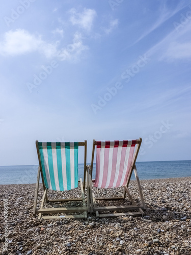 Two deckchairs on pebble beach.