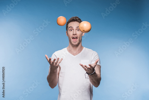 Φωτογραφία Smiling young man juggling with fruits isolated on blue