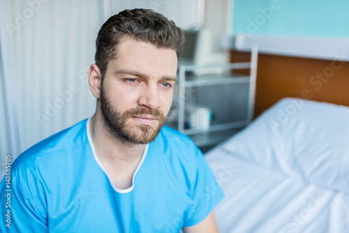 portrait of young sick man sitting on hospital bed, hospital bed patient