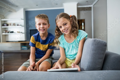 Portrait of siblings with digital tablet sitting on sofa 