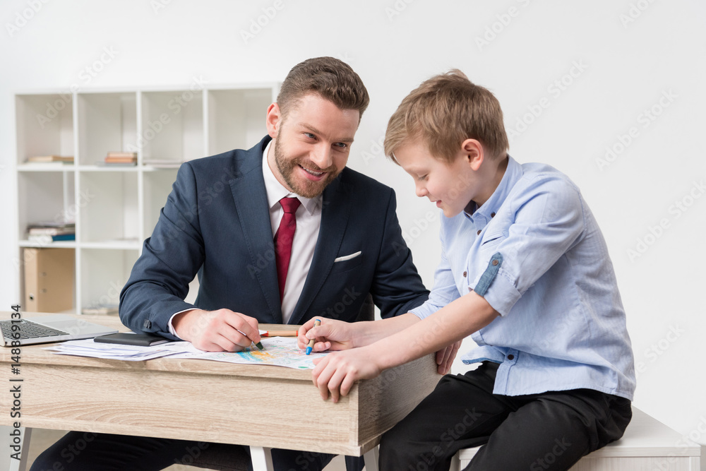 Businessman drawing on business papers with son at office Businessman drawing on business papers with son at office