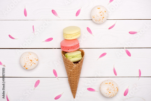Pink flower petals around of handmade fresh macarons in waffle cone on wooden surface. macarons background concept