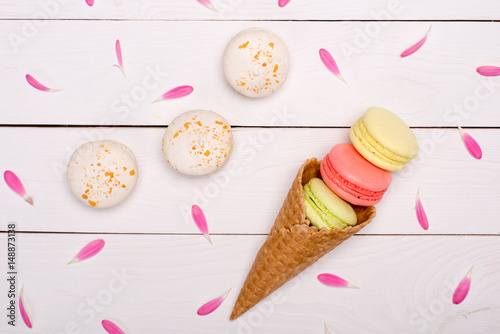 Top view of pink flower petals around handmade fresh macarons in waffle cone. macarons background concept