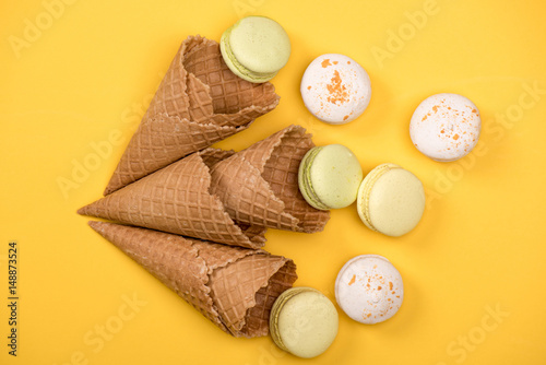 Top view of yellow and white macarons in waffle cones on yellow surface. macarons background concept