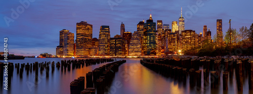New York City Manhattan skyline with skyscrapers over Hudson River illuminated lights at dusk after sunset.