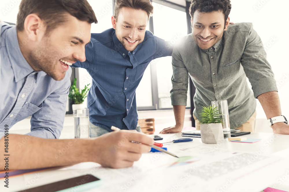 Three young businessmen leaning at table and working at project together, business teamwork concept Three young businessmen leaning at table and working at project together, business teamwork concept