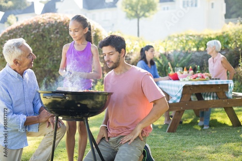 Father and grandfather watching while girl preparing barbecue
