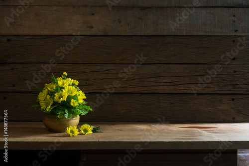 Beautiful yellow flowers with green leaf in the ceramics vase put on the plank in dim light room