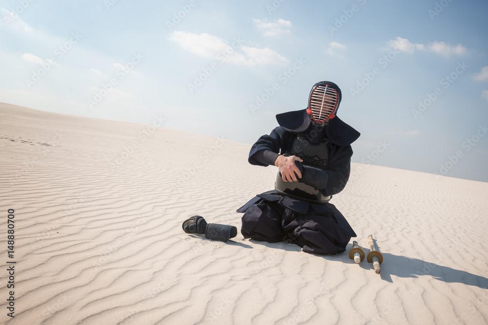 Warrior, man in traditional armor, bogu for kendo sits  in a desert