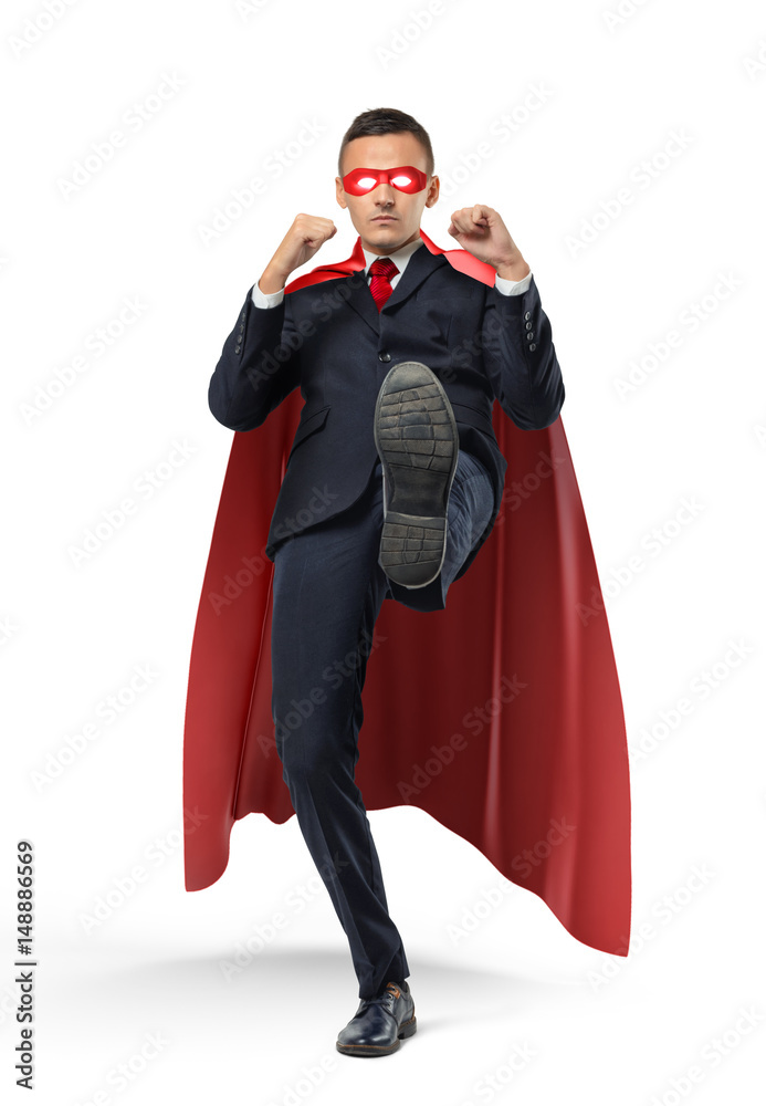 A businessman in a red superhero cape kicking an invisible object on white background. A businessman in a red superhero cape kicking an invisible object on white background.