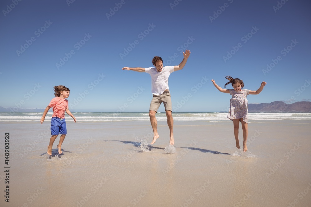 Cheerful father with children jumping on shore at beach Cheerful father with children jumping on shore at beach