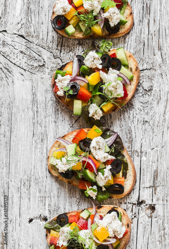 Sandwiches with feta, tomatoes, cucumbers and olives. Greek salad bruschetta style on a rustic board. Delicious appetizer or snack