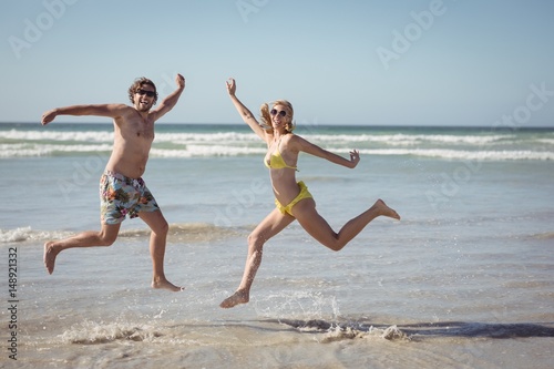 Cheerful couple jumping on shore at beach