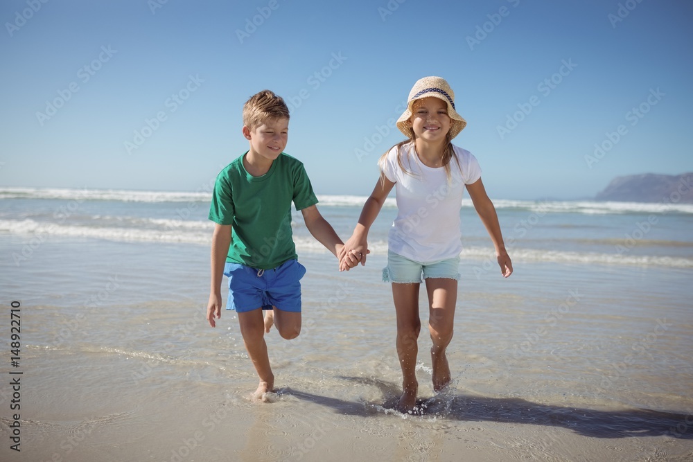 Happy siblings holding hands while running at beach Happy siblings holding hands while running at beach