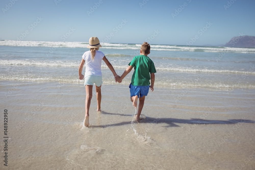 Rear view of siblings holding hands while running on shore Rear view of siblings holding hands while running on shore