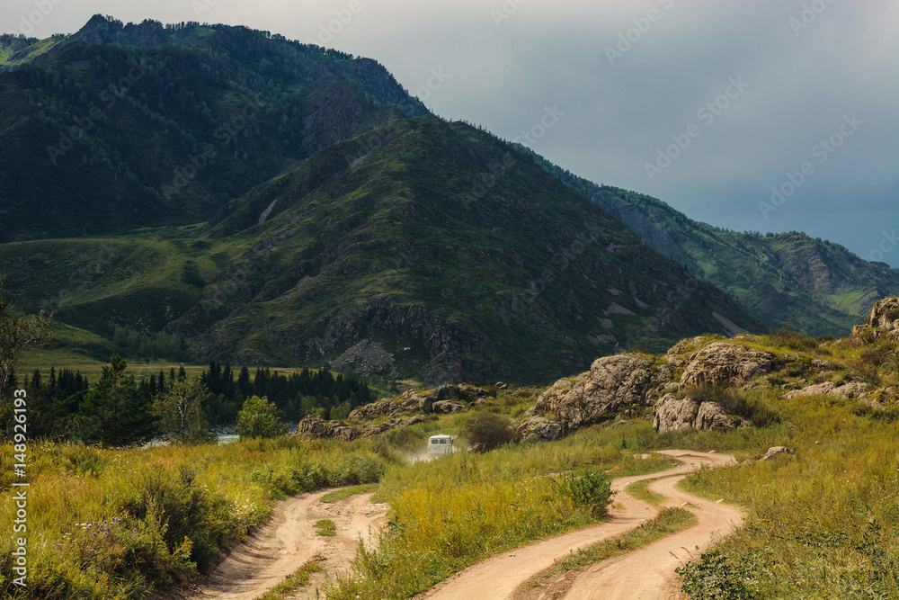 The car is moving forward along a dirt road among the mountains and hills. Mountain Altai.