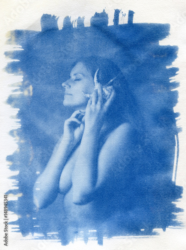 A naked girl with her hair loose listens to the sound of the ocean emitted by the shell.