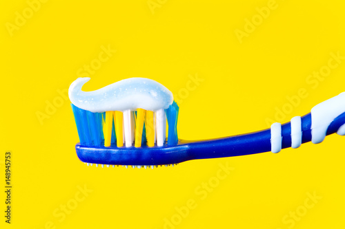 Blue toothbrush with blue toothpaste on a yellow background.