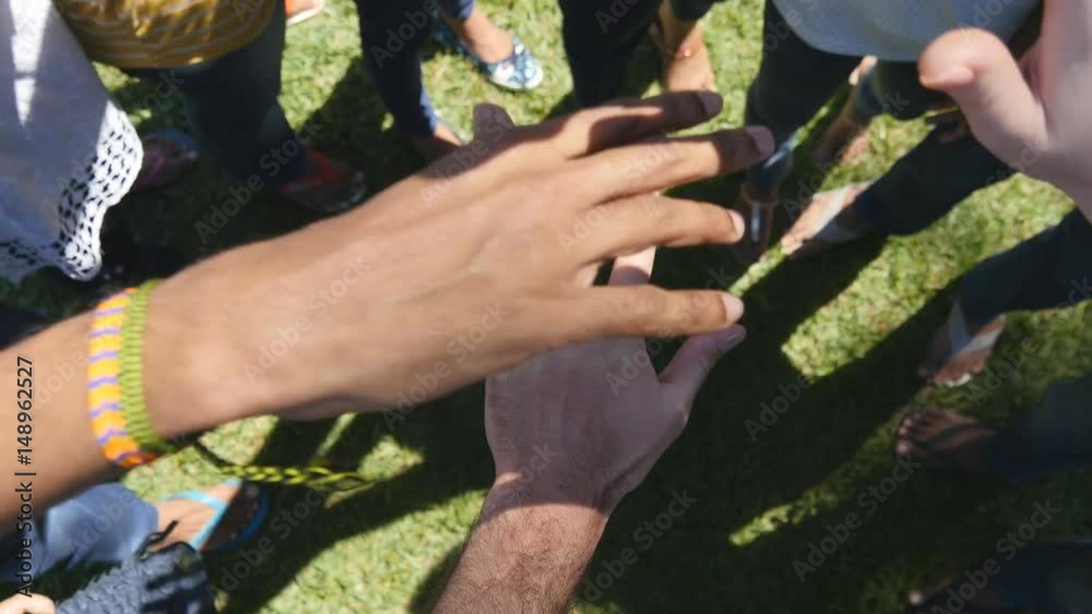 Arm of all races and colors stacked together one by one in unity and teamwork and then raised. Many multiracial hands getting together in the center of a circle and then cheer. Close up outdoor shot
