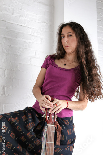 Young brunette woman with acoustic guitar in long skirt. Brick wall background