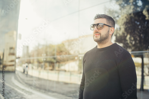 Stylish young business man standing in front his office building on a sunny day.Handsome successful entrepreneur in sunglasses going on a coffee break.Casual dress code corporate policy. Ambitious man © eldarnurkovic