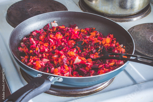 Carrots, beets and onion in a frying pan are roasted on the stove. Ingredients for borsch.