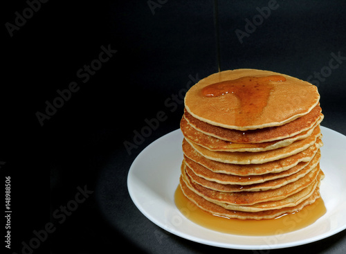 Stack of fresh homemade pancakes with maple syrup served on white plate, black background with free space for text or design 