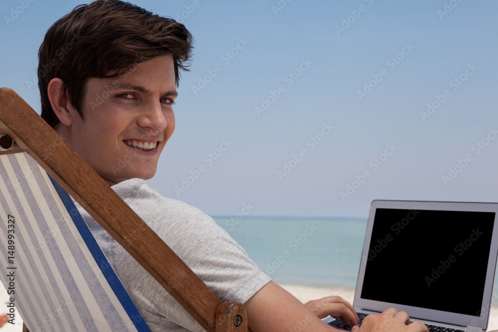 Portrait of young man using laptop at beach