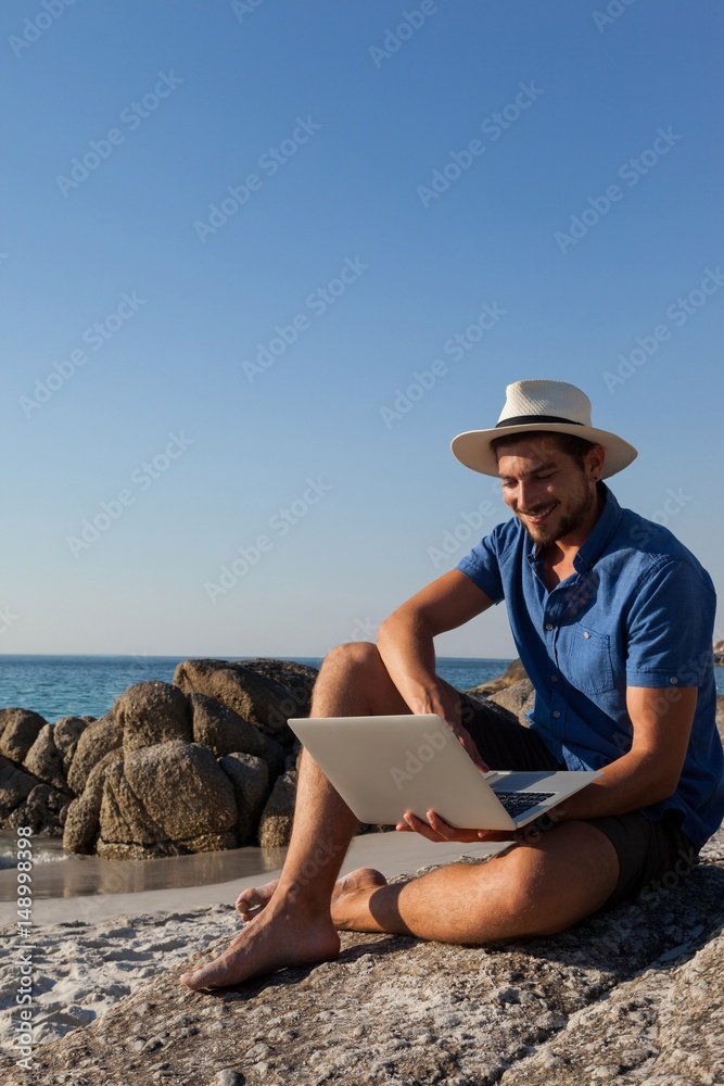 Man sitting on the rocks and using laptop on beach