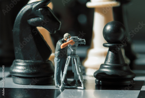 Cameraman miniature doll and chess figures on board. Filming the checkmate game. photo