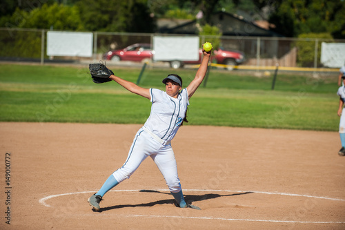 White uniform fast pitch softball pitcher winding up to throw in side view.  © motionshooter