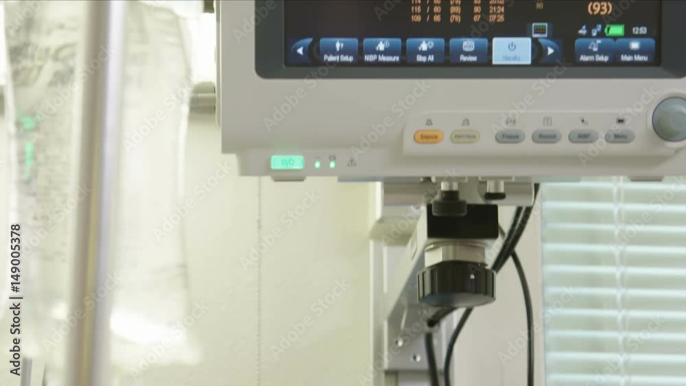 Tilt up from an IV bag to a vital signs monitor in a hospital, measuring heartbeat (pulse), blood pressure and oxygen. Shot in 4K UHD.