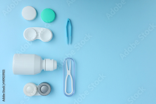 Cases for contact lenses, tweezers and bottle of solution on blue background