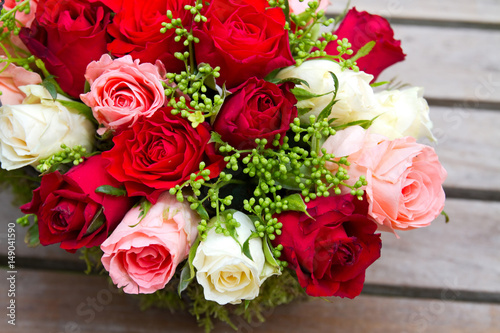  Rosengesteck mit roten  rosafarbenen und wei  en Rosen auf einem Holztisch