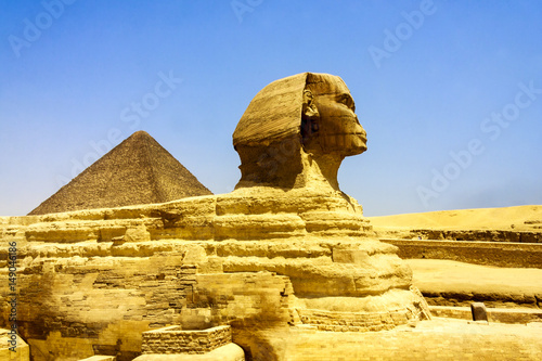 Close up of the face of the Great Sphinx with a set of pyramids in the background on a beautiful clear blue sky day in Giza, Cairo, Egypt 
