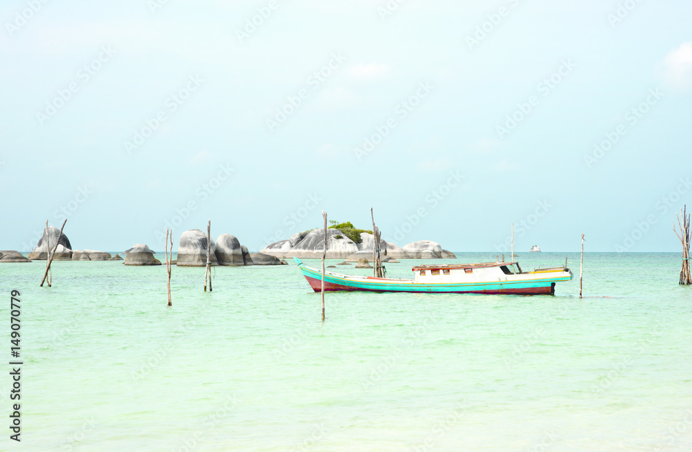 Empty fishing boat docked at the turquoise colored ocean coast near white sand beach in the afternoon with rocks on the ocean horizon in Belitung, Indonesia Empty fishing boat docked at the turquoise colored ocean coast near white sand beach in the afternoon with rocks on the ocean horizon in Belitung, Indonesia